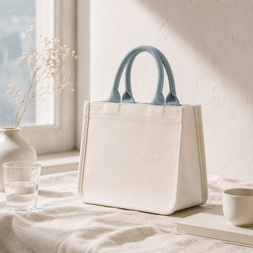 Mini canvas tote in ivory cotton canvas with mist blue handles, soft structured shape and flat bottom.