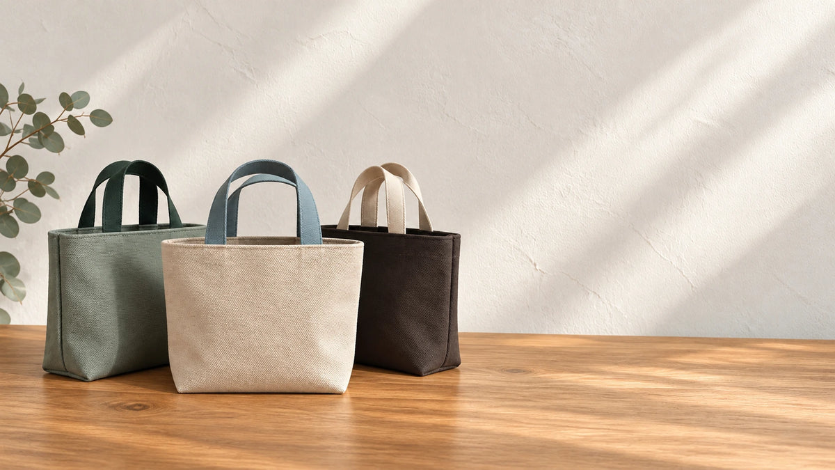 Three Mini Canvas Totes in Dune, Forest and Umber on a wooden table.