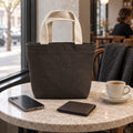 Umber Mini Canvas Tote at a cafe beside a phone, wallet and coffee cup.